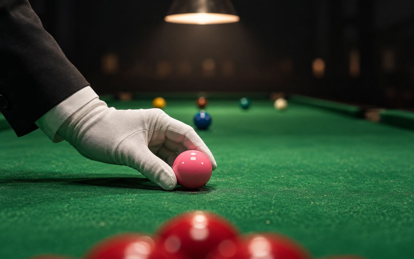 Referee's gloved hand placing the pink ball on its spot on a lit snooker table